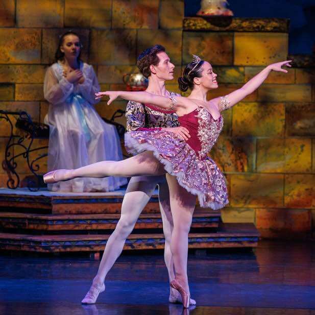 A male and female ballerina dressed in themed costumes perform a duet together on stage.