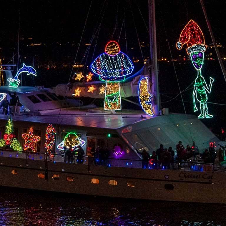 A boat floats in the darkened Santa Barbara Harbor, illuminated by bright holiday lights and themed decor.